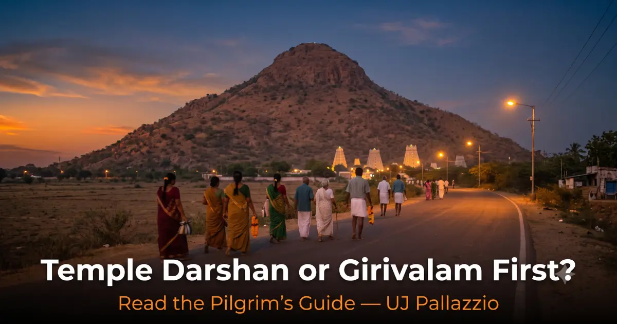 Pilgrims walking barefoot along the Girivalam path at dusk, with Arunachala Hill ahead and the lit gopurams of Arunachaleswarar Temple at its base, Tiruvannamalai